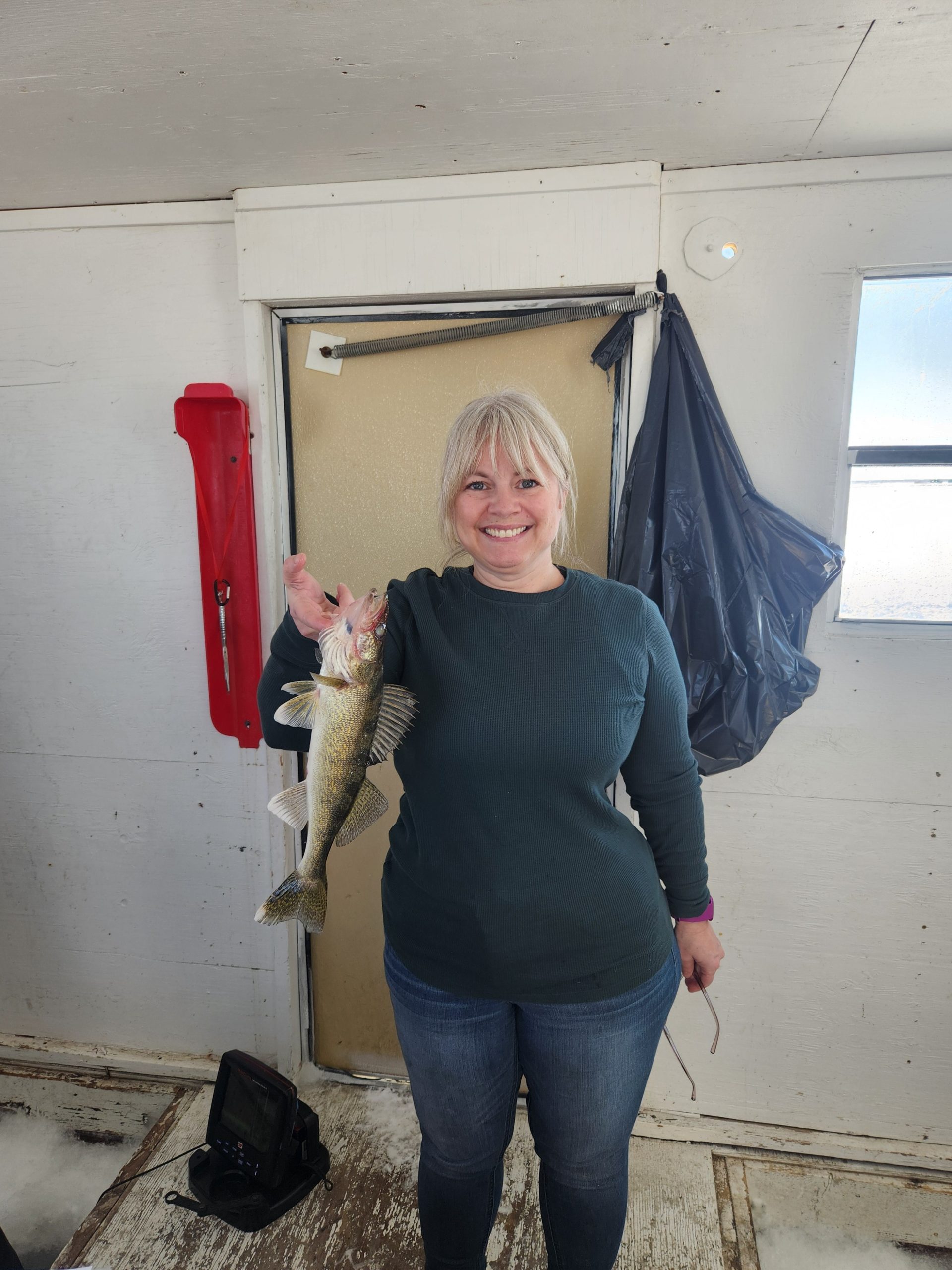 Gretchen Enger holding a walleye caught ice fishing, smiling inside a fishing house